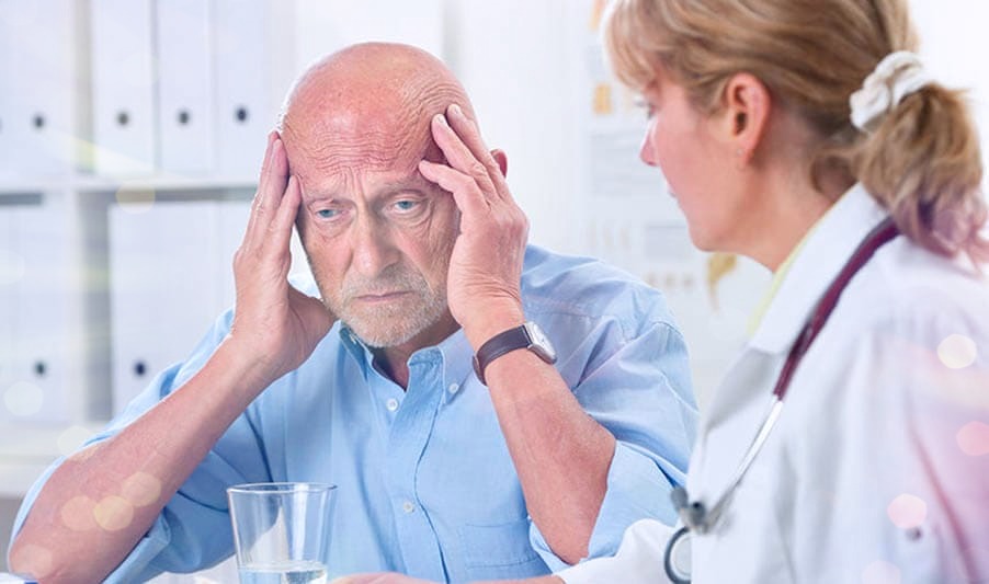 Пожилой мужчина в кабинете врача держится за голову