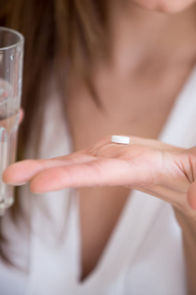 Девушка держит в одной руке стакан в другой таблетку